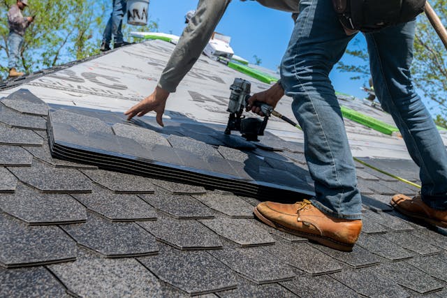 Roofer using nail gun for shingle installation 